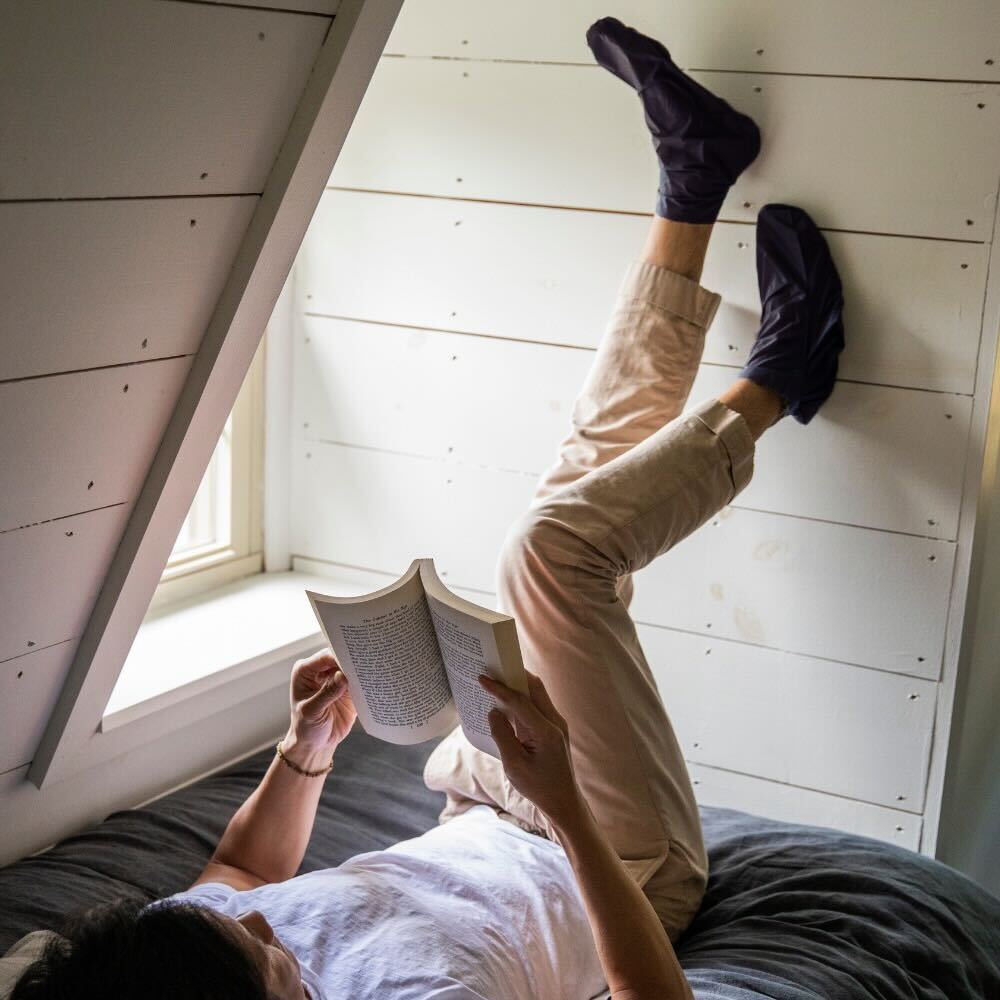 Man sitting on bed with hydrating foot mask on while reading a book